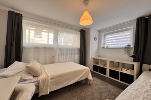 A bedroom with two beds, a bedside table, a lamp, a window with blinds, and a hanging light fixture. - Kühlungsborn - SeaSide No. 6 (Kuehlungsborn)