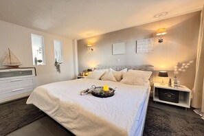 A neatly arranged bedroom with a bed, bedside tables, wall-mounted lamps, and a decorative sailboat. - Kühlungsborn - SeaSide No. 6 (Kuehlungsborn)