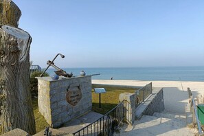 Un monument en pierre avec une plaque commémorative, une sculpture en métal et une vue sur la plage et l’océan.