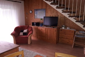 A wooden interior with a red armchair, a television on a wooden cabinet, and a staircase. - Holiday home with 1 bedroom (Norden-Norddeich)