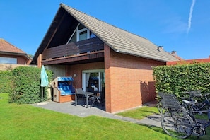 A single-story house with a sloped roof, a patio with outdoor furniture, and a bicycle parked outside. - Holiday home with 1 bedroom (Norden-Norddeich)