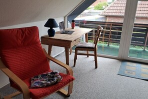 Ein Zimmer mit einem roten Sessel, einem Holztisch, einem Laptop und einer roten Tasse.
