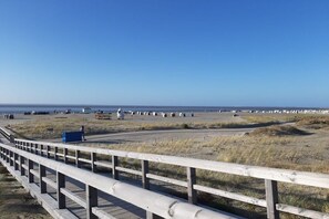 A coastal walkway with a wooden railing, leading to a beach area with dunes and a clear sky. - Holiday home with 1 bedroom (Norden-Norddeich)