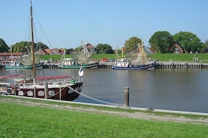 A harbor with boats docked, a grassy area, and houses in the background. - Holiday home with 1 bedroom (Norden-Norddeich)