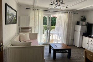 Habitació amb un llit, una taula, una petita cuina i una porta corredissa de vidre que dona a una zona exterior.