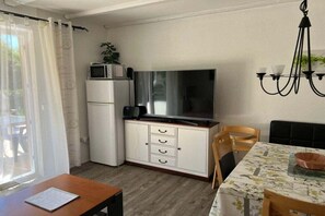 A compact living space with a kitchenette, a flat-screen TV, a dining table with chairs, and a window with curtains. - Holiday apartment with 1 bedroom (Arrach)