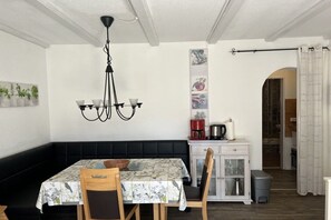A dining area with a table set for two, a black cushioned bench, a chandelier, and a cabinet with kitchen appliances. - Holiday apartment with 1 bedroom (Arrach)