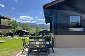 Eine Holzhütte mit einer Terrasse, Sitzgelegenheiten im Freien und Blick auf die umliegende Landschaft.