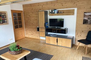 A modern living room with a flat-screen TV, wooden cabinets, a bookshelf, and a potted plant. - Holiday apartment with 1 bedroom (Bischofswiesen)