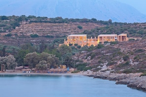 A coastal property with a large building, a beach with umbrellas, and a mountainous backdrop. - Olea Villas - Amazing villas by the sea (1) (Chania)