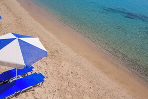 En strand med klart vand, en blå og hvid parasol og en blå liggestol.