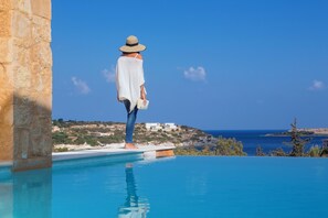 A person standing at the edge of a pool with a clear view of the sea and a hilly landscape in the background. - Olea Villas - Amazing villas by the sea (1) (Chania)