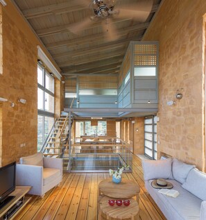 A spacious interior with a high ceiling, wooden floors, a staircase leading to an upper level, and a seating area with a television. - Olea Villas - Amazing villas by the sea (1) (Chania)