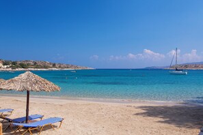 A beach with clear blue water, a boat in the distance, and a straw umbrella. - Olea Villas - Amazing villas by the sea (1) (Chania)