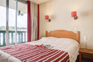 Une chambre d’hôtel avec un lit, une table de chevet, une couvre-lit à rayures rouges et blanches, deux lampes fixées au mur et une vue sur l’extérieur.