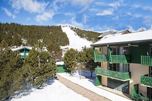 A snow-covered mountain with a ski slope, a building with green balconies, and a clear blue sky. - 100m from ski slopes, parking, ski locker, 35m², Pyrénées 2000 (Pyrénées 2000)