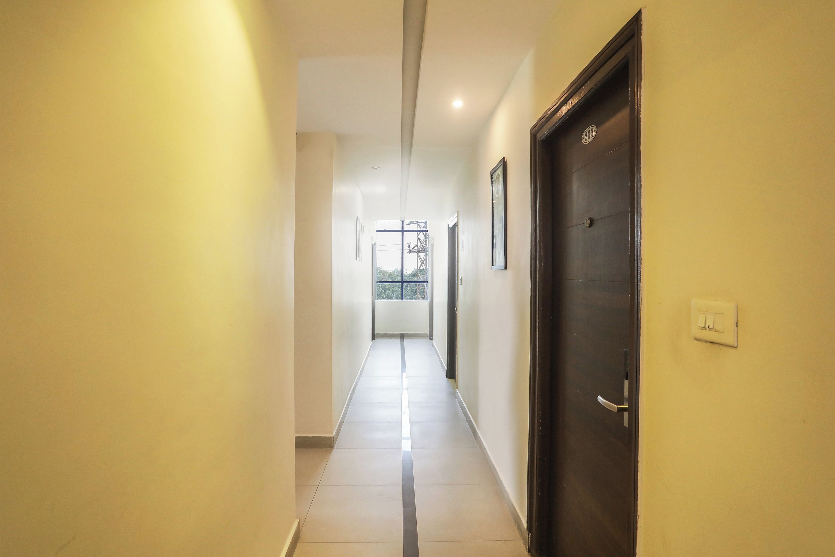 Corredor com uma porta à direita, um interruptor de luz e uma janela no final.