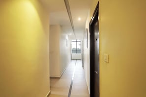 A corridor with a door on the right, a window at the end, and a light switch on the wall. - Collection O SSR Royal Suites (Hyderabad)