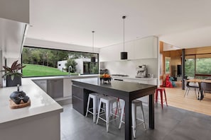 A modern kitchen with a large island, stainless steel appliances, and a view of the outdoors. - Cedar | Treetop Estate with Solar Heated Pool (Mount Eliza)