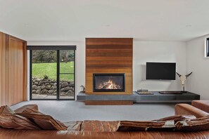 A modern living room with a fireplace, a television, and a stone wall. - Cedar | Treetop Estate with Solar Heated Pool (Mount Eliza)