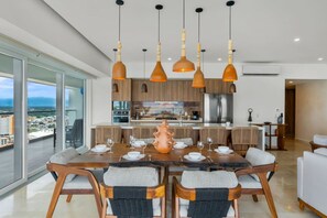 A modern dining area with a large table, chairs, and pendant lights. - Harbor N2301 by Moikkarentals (Puerto Vallarta)