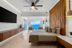 Een moderne slaapkamer met een groot bed, een plafondventilator, een televisie en uitzicht op zee.