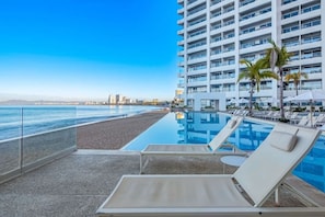 A poolside area with lounge chairs and a view of the ocean. - Luxury Beachfront Condo at Harbor 171 N1409  Puerto Vallarta (Puerto Vallarta)