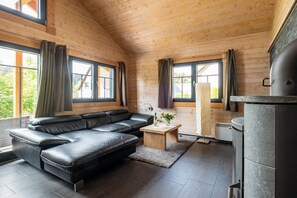 Ein modernes Interieur einer Blockhütte mit einem Ecksofa, einem kleinen Holztisch und einem Kamin aus Stein.