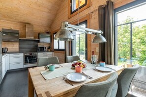 A wooden interior with a dining table set for four, a kitchen with modern appliances, and large windows offering a view of greenery. - Holiday home in Schierke with sauna (Schierke)
