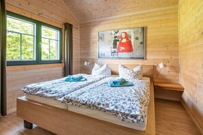Ein Schlafzimmer einer Holzhütte mit zwei Betten, einem Bild an der Wand und einem Fenster mit Vorhängen.