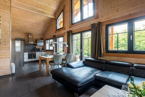 A modern log cabin interior with a dining area, kitchen, and a large black leather sofa. - Holiday home in Schierke with sauna (Schierke)