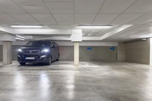 A parking garage with a car parked in a spot, concrete pillars, and a clean, tiled floor. - Holiday apartment House Finja 322259 (Kühlungsborn)