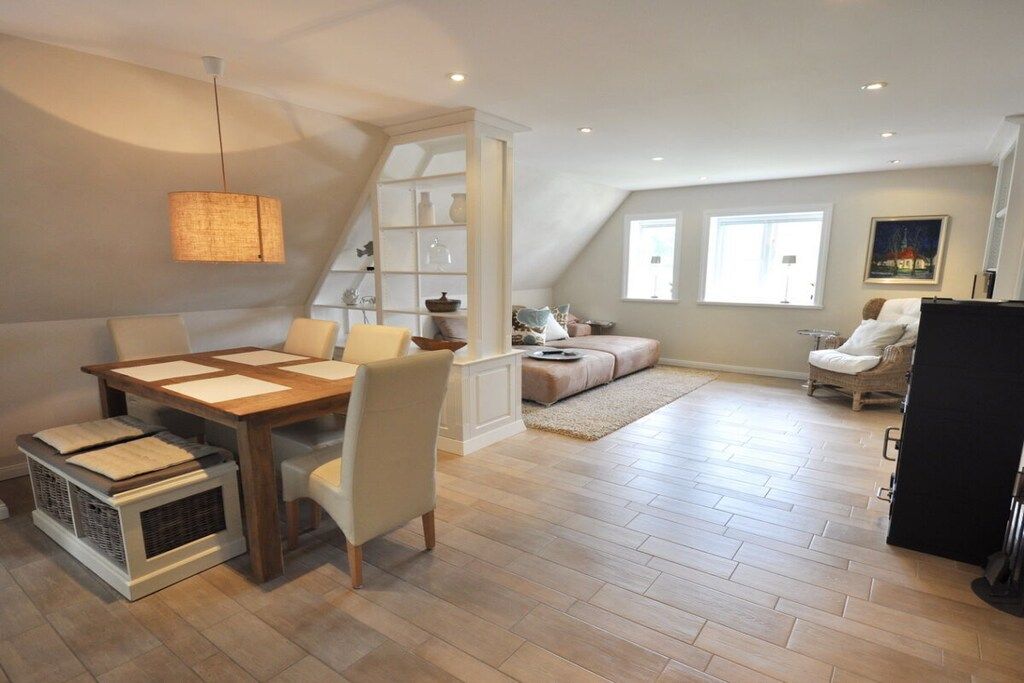 A spacious loft with a dining area, a built-in bookshelf, a cozy seating area, and a large window providing natural light.