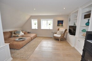 A living room with a brown sofa, a white armchair, a television, and a fireplace. - Old Rectory 5||St.Peter-Ording (St.Peter-Ording)