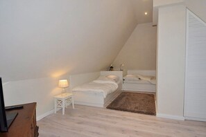A bedroom with a sloped ceiling, a bed, a nightstand with a lamp, and a wooden dresser. - Old Rectory 5||St.Peter-Ording (St.Peter-Ording)