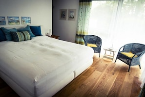A hotel room with a large bed, two wicker chairs, a small table, and artwork on the wall. - Holiday apartment with 1 bedroom (Kressbronn)