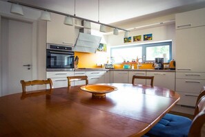 Een moderne keuken met witte kasten, een inbouwoven, een eettafel met stoelen en een raam dat natuurlijk licht toelaat.