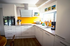 A modern kitchen with white cabinets, a yellow accent wall, and a window providing natural light. - Holiday apartment with 1 bedroom (Kressbronn)