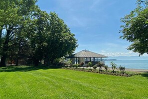 A gazebo with a glass roof overlooking a body of water, surrounded by lush greenery and trees. - Holiday apartment with 1 bedroom (Kressbronn)