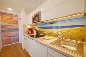 A modern kitchen with a stainless steel sink, a microwave, and a backsplash with a landscape design. - Seestern 9 Apartment House Seestern (Norderney)