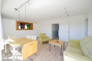 Una sala moderna con una mesa de comedor de madera, dos sillones, un sofá y un televisor montado en la pared.