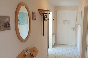 Um corredor com uma porta branca, um espelho fixado na parede e um pequeno prateleira com um porta-retrato.