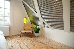 Ein Zimmer mit schrägen Wänden, einem Holzstuhl, einem Topfpflanzen und einem gemusterten Teppich.