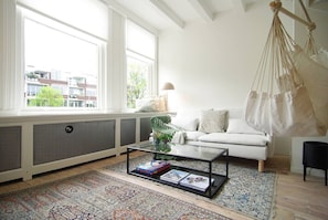 A living room with a sofa, a hanging chair, a coffee table, and a large window. - Historic Townhouse close to Waterloo square and Botanic Gardens (Amsterdam)