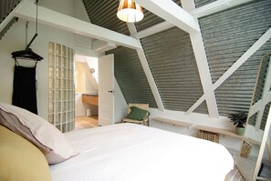 A bedroom with a sloped ceiling, a bed, a hanging light fixture, and a chair. - Historic Townhouse close to Waterloo square and Botanic Gardens (Amsterdam)