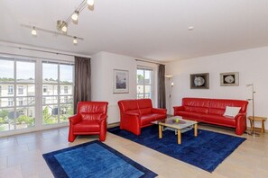A spacious living room with a large window, red leather sofas, a coffee table, and a blue rug. - Holiday apartment Haus Olymp 319676 (Kühlungsborn)