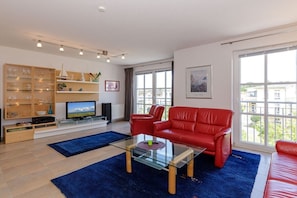 A living room with a glass coffee table, red leather sofa, and a television on a stand. - Holiday apartment Haus Olymp 319676 (Kühlungsborn)