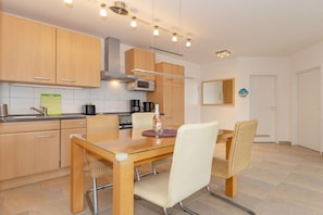 A modern kitchen with wooden cabinets, a glass dining table, and two wicker chairs. - Holiday apartment Haus Olymp 319676 (Kühlungsborn)