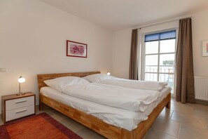 Ein Schlafzimmer mit einem Doppelbett, einem Nachttisch mit Lampe, einem gerahmten Bild an der Wand und einem Fenster mit Vorhängen.