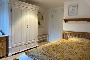 Ein Schlafzimmer mit einem Bett, einem Kleiderschrank, einer Bank und einem an der Wand befestigten Regal.